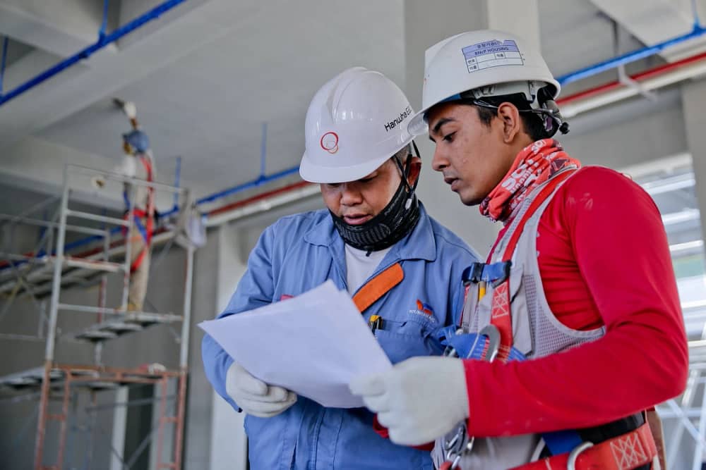 Two people wearing white hard hats look over a construction proposal. 