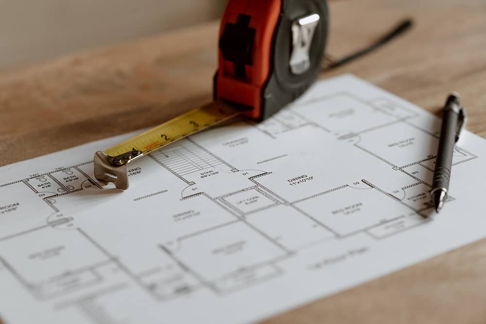 A black pen and measuring tape lays over a black and white blueprint.