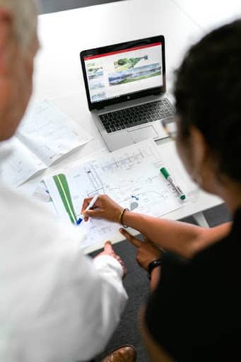 Two people working on a building layout in front of an open laptop.