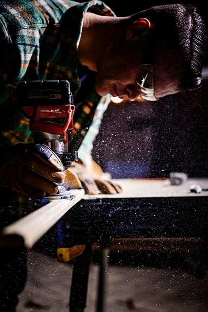 A carpenter wearing safety glasses sanding a piece of wood.