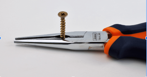 A close-up of orange and black pliers holding a bronze screw upright.