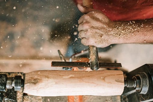 A carpenter carving a rotating piece of wood.