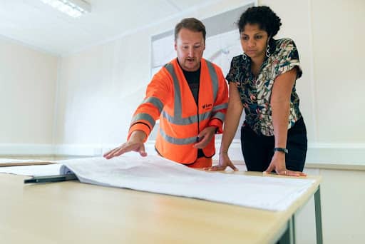 Two people planning a construction project on a large white blueprint.