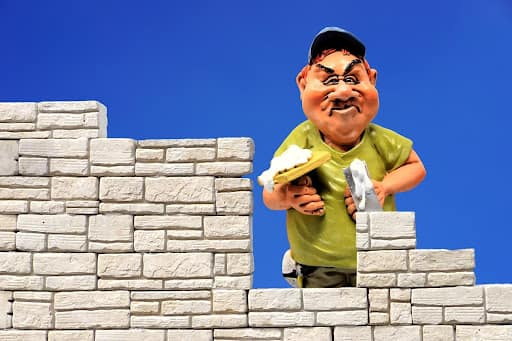 A construction worker made of clay building a tan brick wall on a blue background.