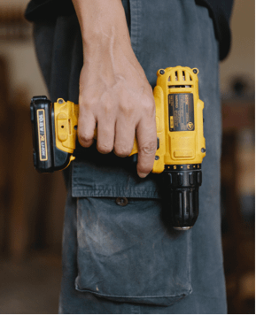A person wearing navy blue cargo pants holding a yellow drill by their waist.