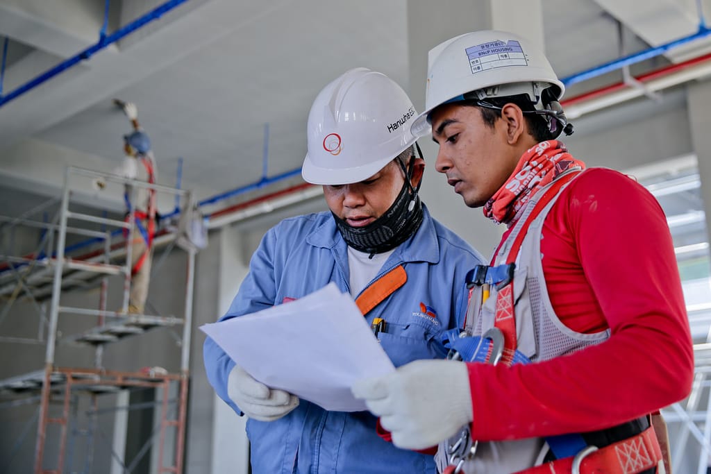 Two people in white hard hats at a worksite looking at a piece of paper and discussing its contents.